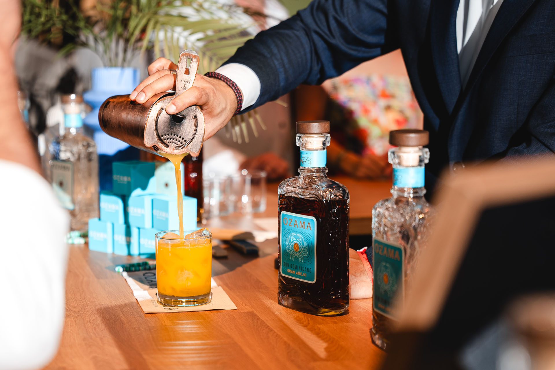 A bartender pours a vibrant orange drink into a glass, surrounded by bottles of rum and a stylish bar setup.
Title: /