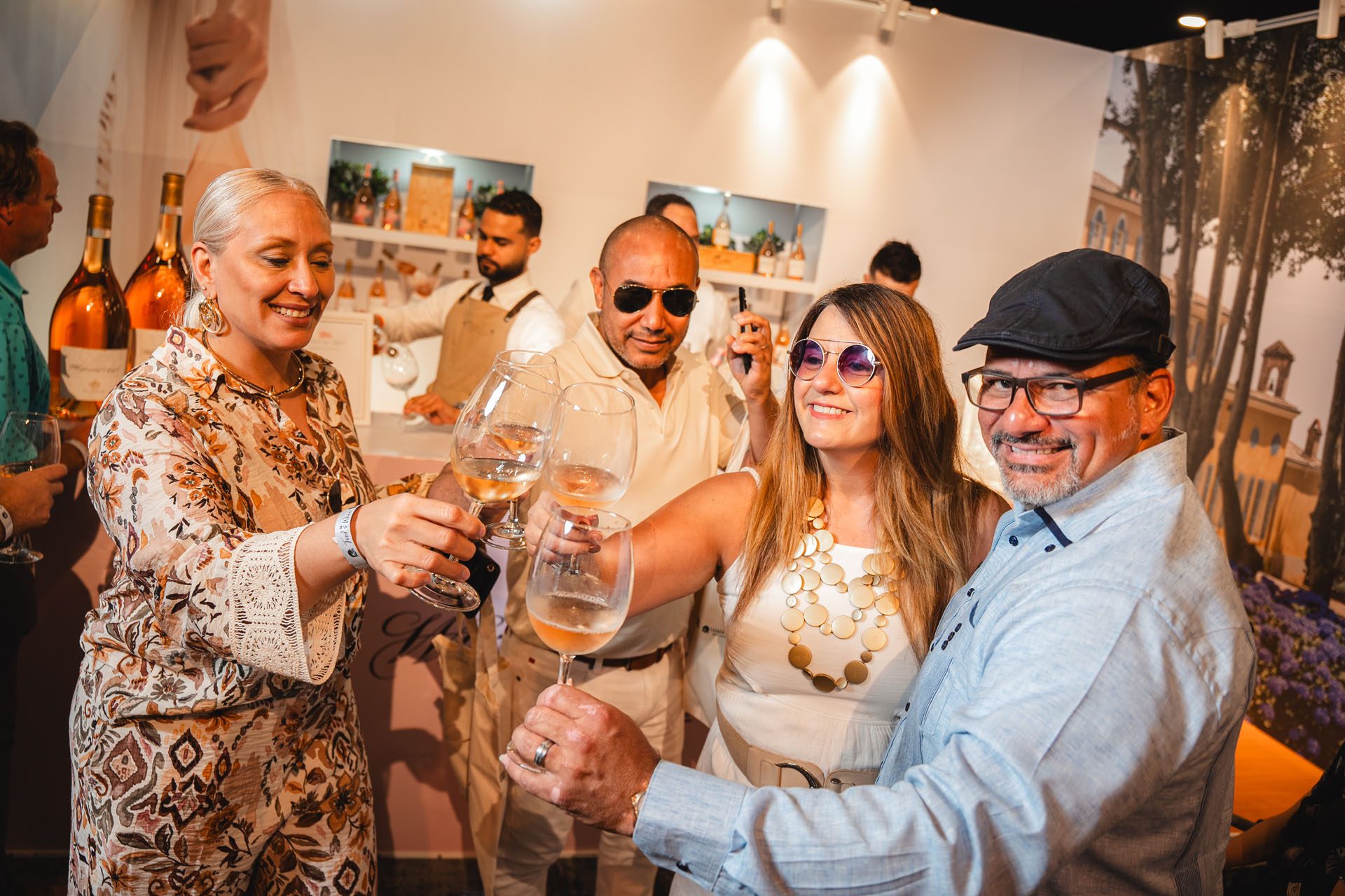 A group of four people toast with wine glasses at a social event, smiling and enjoying the moment. A bartender is visible in the background.